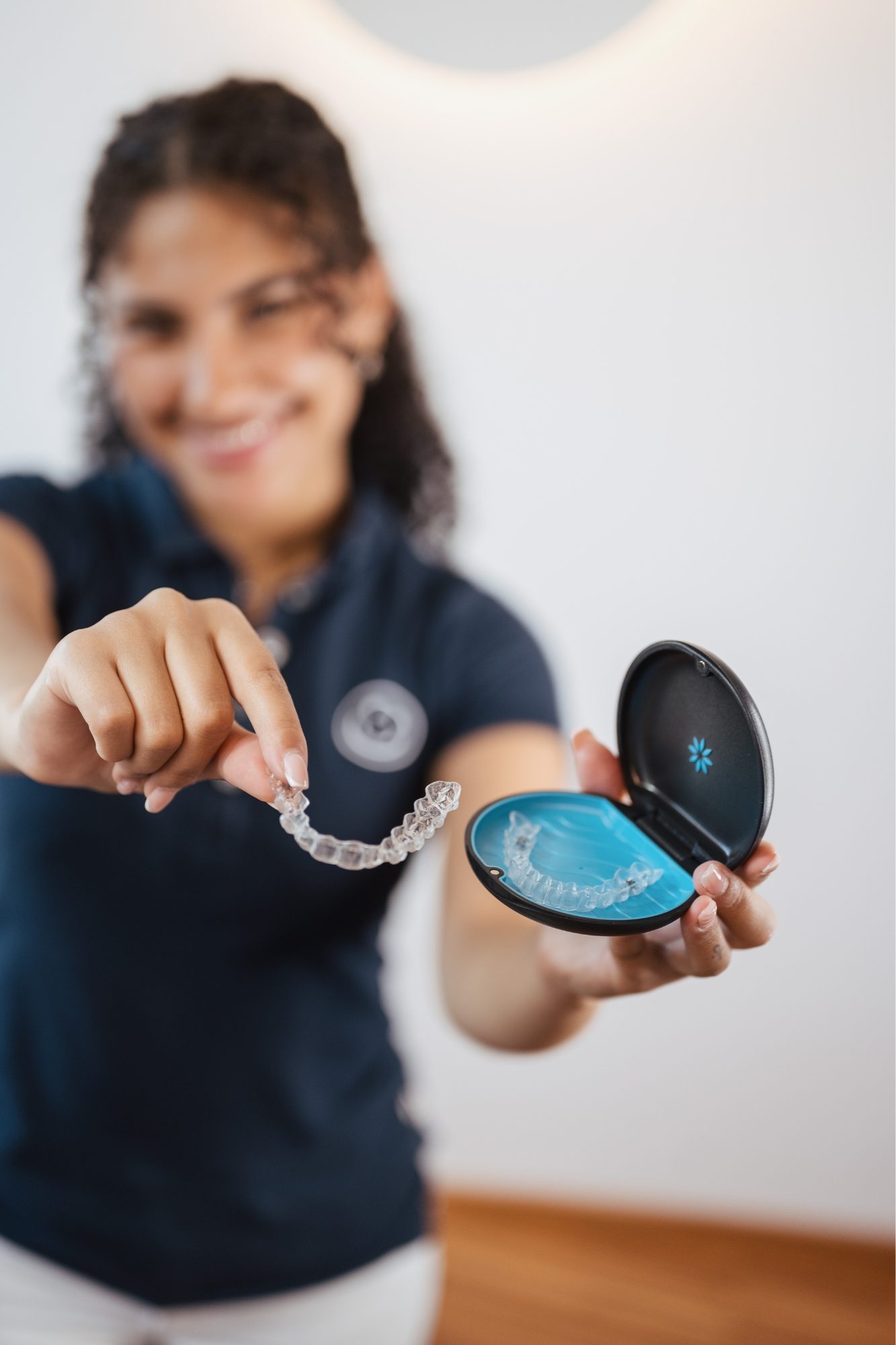 Eine junge Frau hält ihren Invisalign-Behälter in die Kamera und lächelt.
