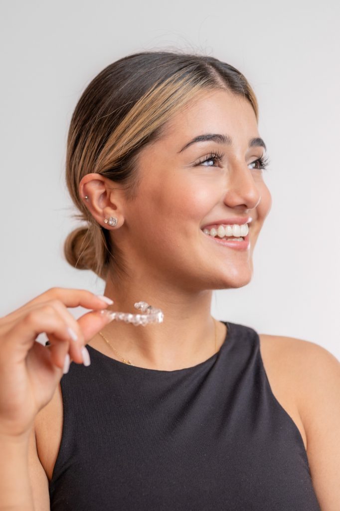 Eine junge Frau hält ihre Invisalign-Schiene in der Hand und zeigt ihr perfektes Lächeln.